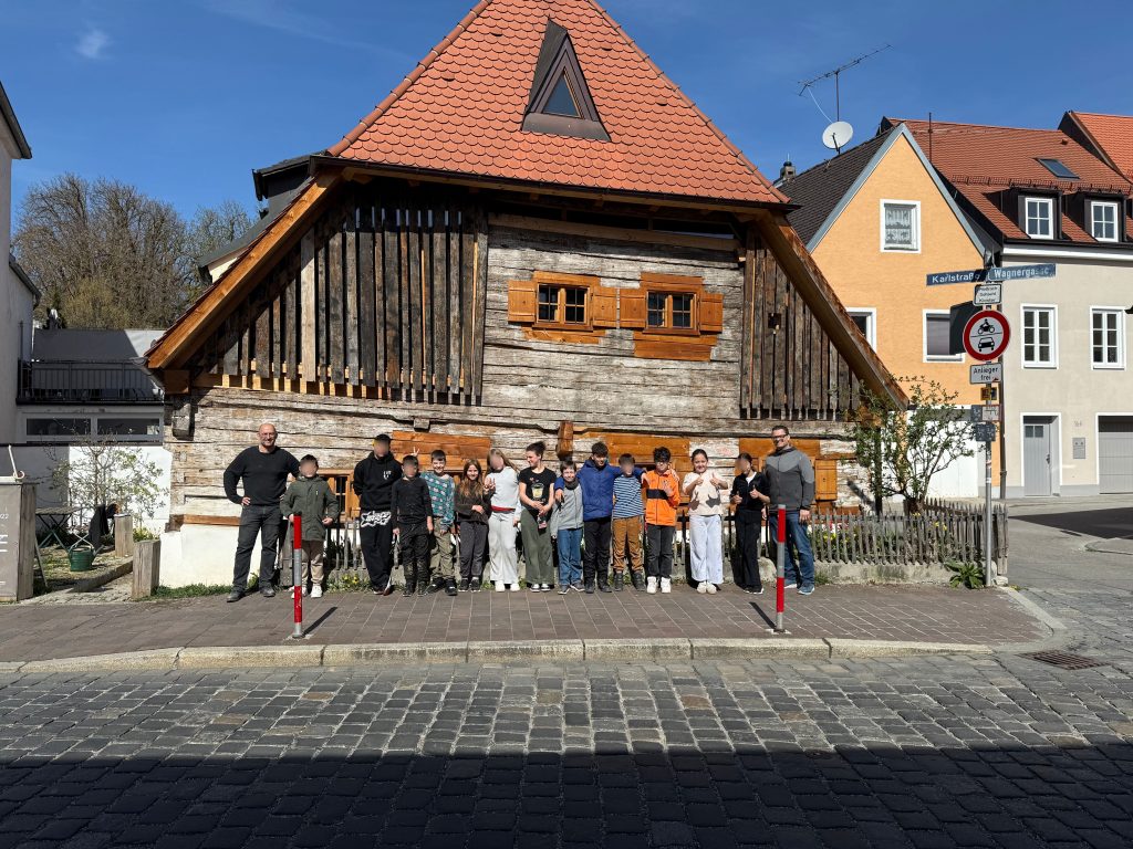 Schüler der Klasse 5a positionieren sich auf einem Gruppenfoto mit dem Architekten Hr. Stenger und der betreuenden Lehrkraft Herr Sauter vor einem historischen Haus für ein Gruppenfoto